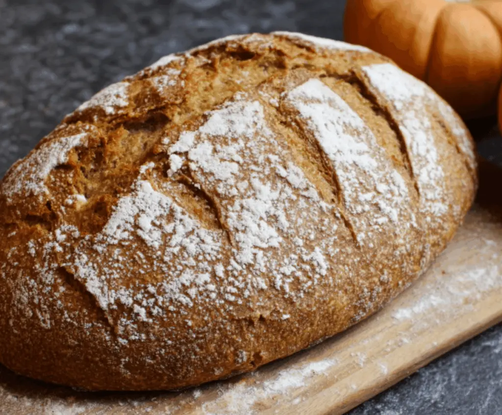 Golden-brown pumpkin sourdough bread loaf with a crusty exterior and swirls of pumpkin, perfect for fall baking and holiday gatherings.